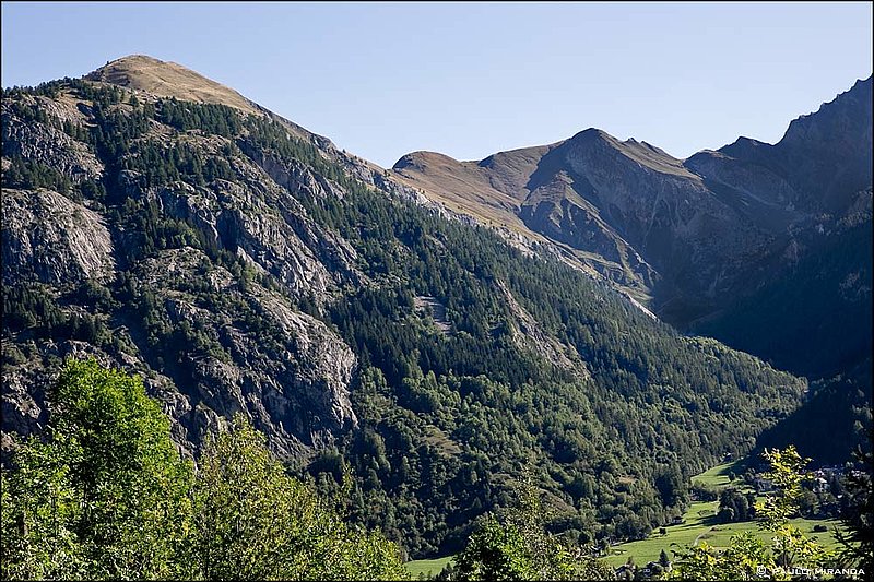 Depois do Col Chècrouit, tem-se uma visão integral da encosta a subir no dia seguinte: a TMB ziguezagueia pelo trecho arborizado entre a encosta rochosa à esquerda e o fundo do vale. O Refúgio Bertone é o ponto branco no canto superior esquerdo.